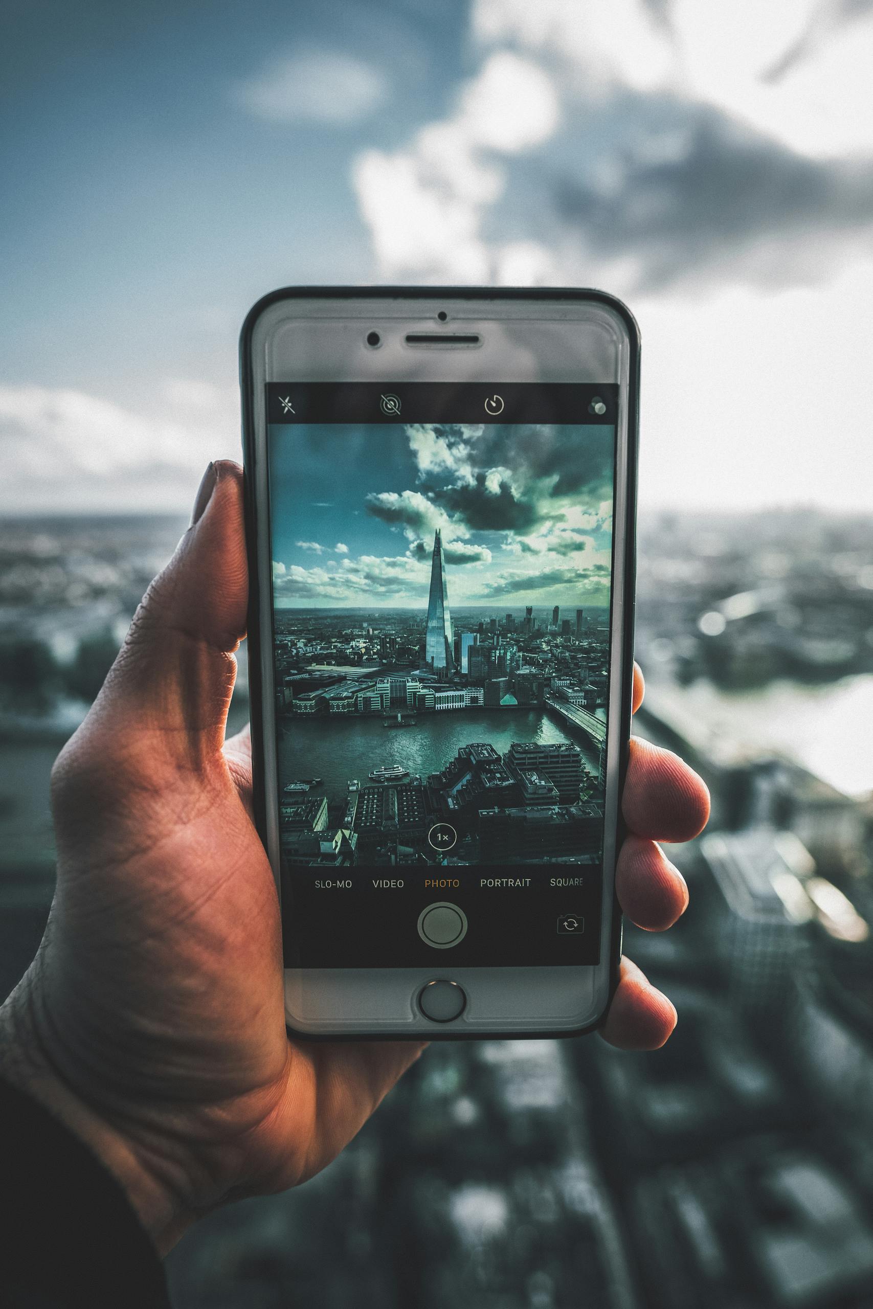 A hand holding a smartphone taking a photo of The Shard skyscraper in London.