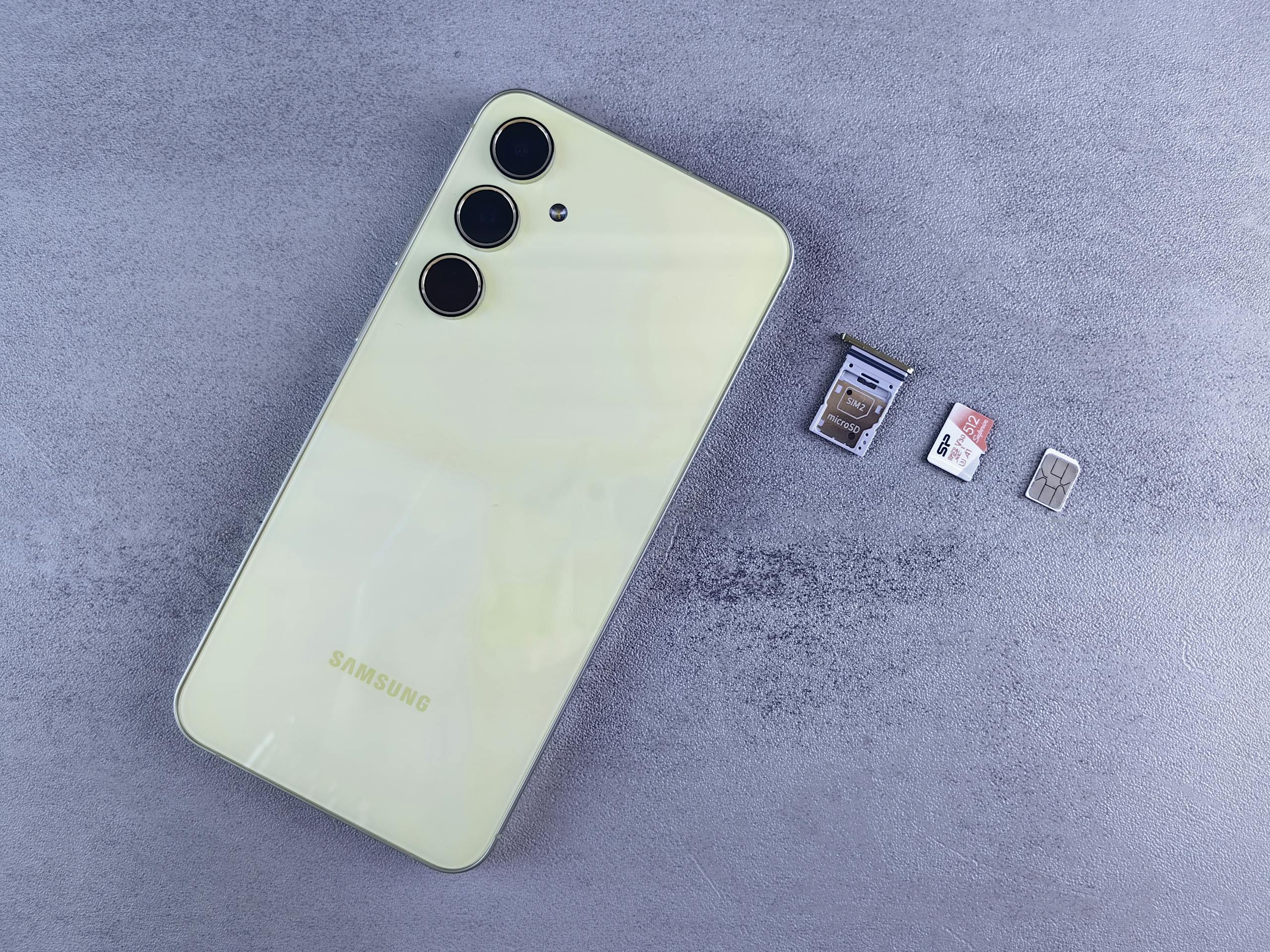 Yellow smartphone with SIM tray, memory card, and SIM card on gray background.